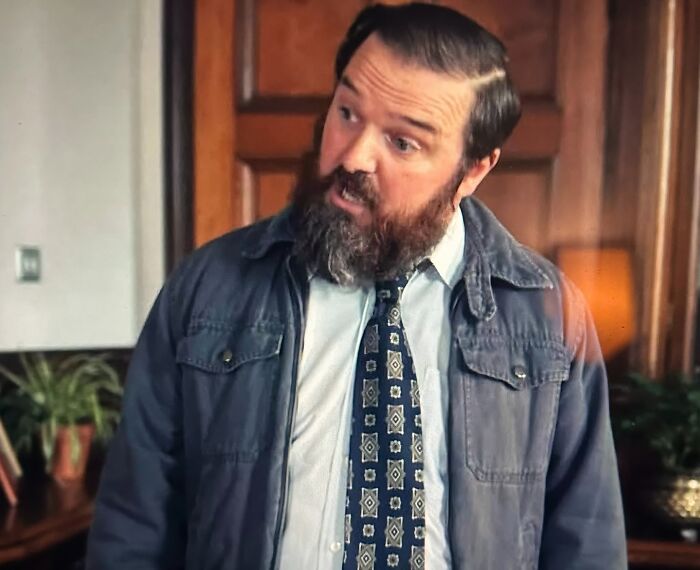 Man with a beard wearing a patterned tie and jacket, reacting emotionally to one of the most tragic losses in TV shows.