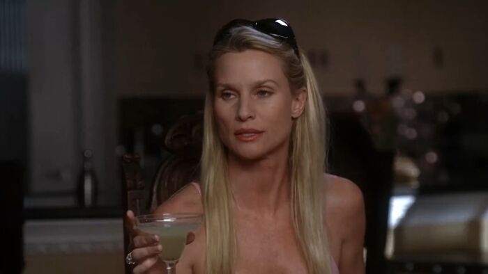 Blonde woman holding a cocktail glass, sitting indoors with a reflective expression, symbolizing tragic losses in TV shows.