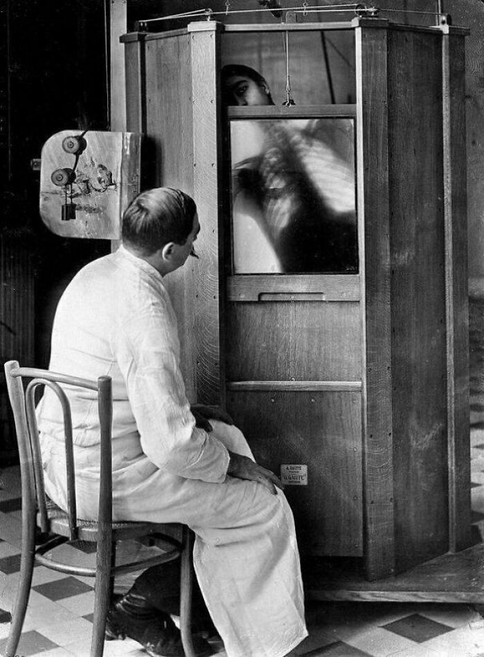 Man in white coat examining a vintage medical X-ray machine showing a chest scan in a historic medical setting.