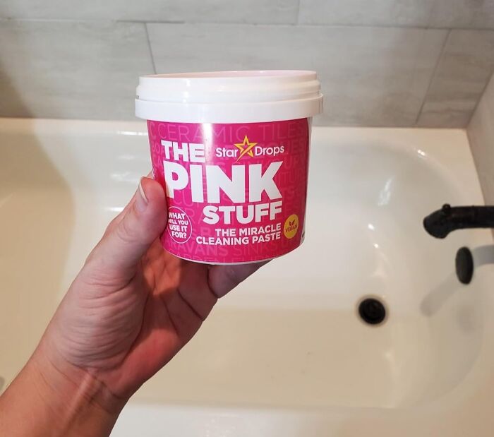 Hand holding a container of pink cleaning paste over a white bathtub, illustrating genius ways to fix little glitches.