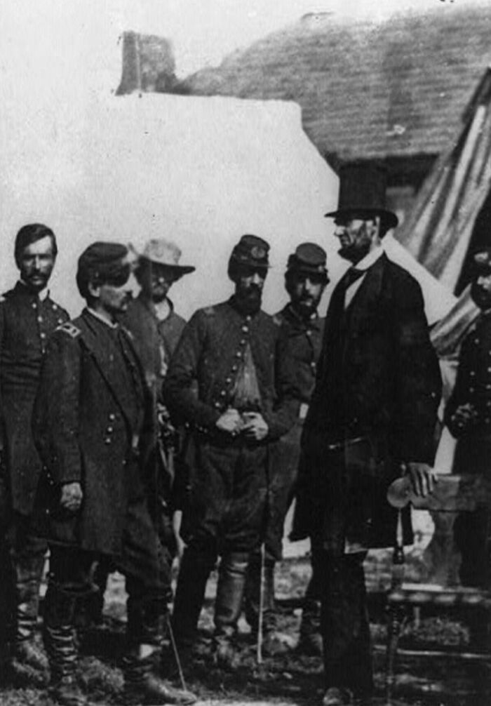 Black and white historical photo showing Abraham Lincoln with Union soldiers during the American Civil War era.