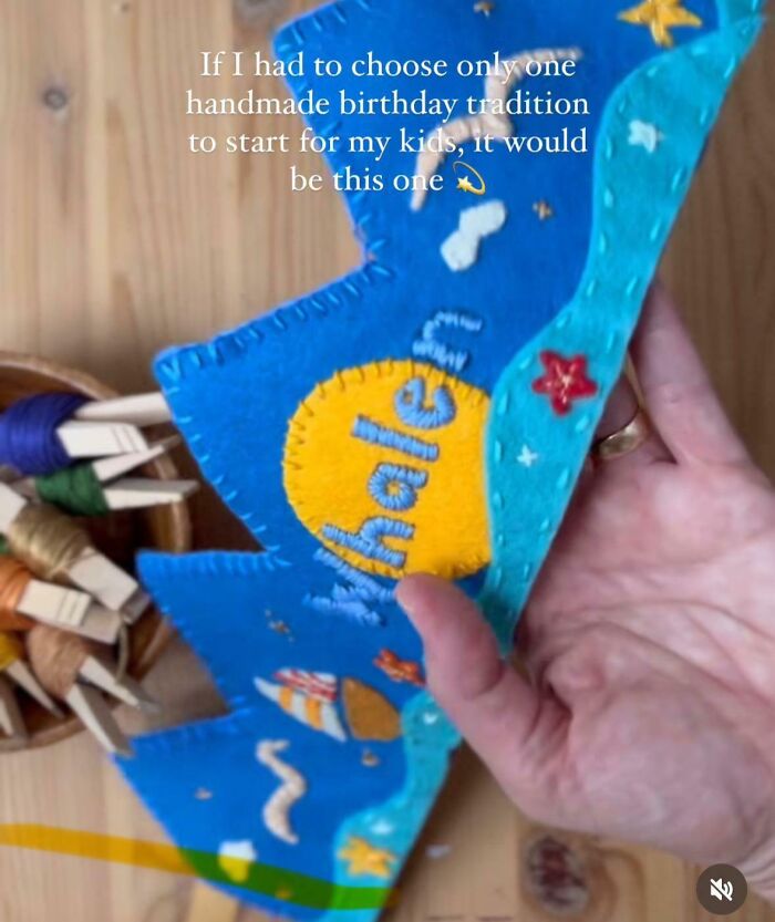 Hand holding a colorful handmade felt craft with embroidered details, related to popular baby names and parenting traditions.