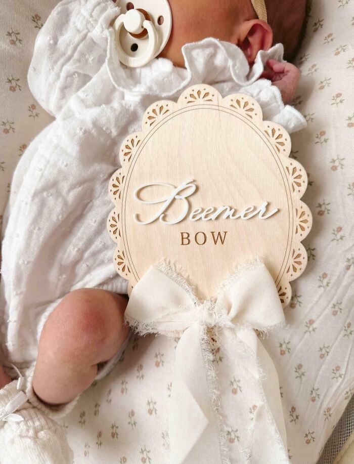 Newborn baby wearing white outfit, lying beside a decorative wooden sign and bow, highlighting unique baby names.