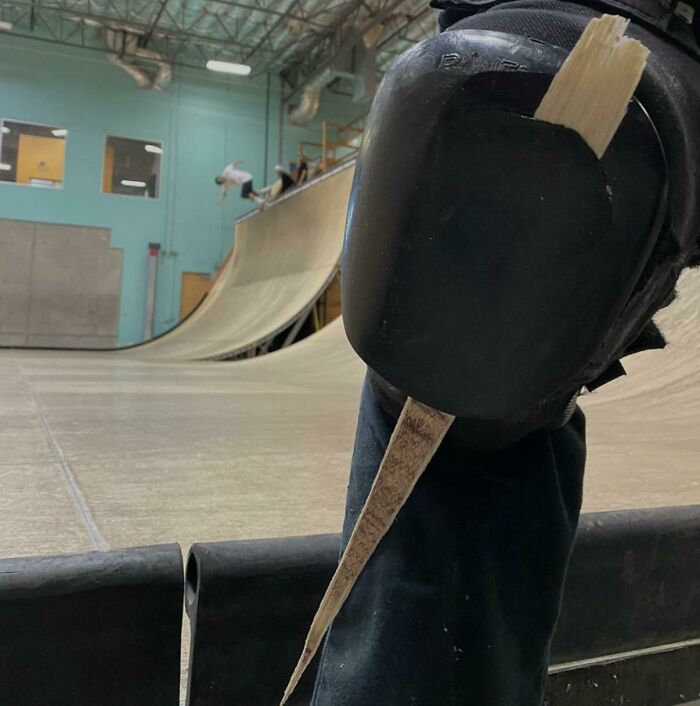 Close-up of a person’s knee pad with a c*****d wooden stick stuck in it at a skatepark, showing unbelievable luck.