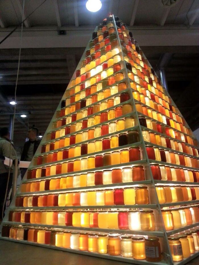 Pyramid display of colorful jars showcasing variety in spices and preserves under indoor lighting with people nearby.