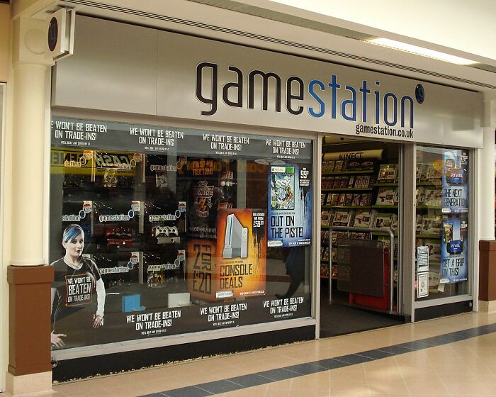 GameStation storefront in a mall, featuring console deals and promotional posters for trade-in offers and video games.