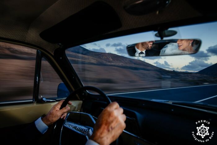Couple smiling in rearview mirror while driving down a scenic road in an unforgettable wedding photo.