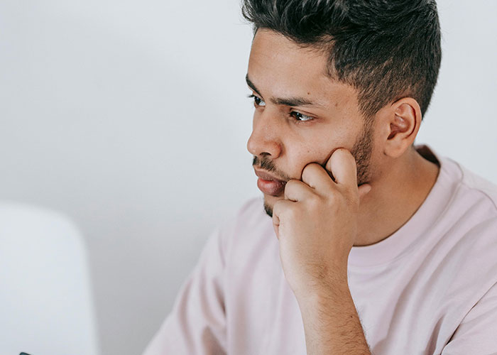 Young man in a pink shirt looking thoughtful and concerned, reflecting on wife cheating and mind-control excuse.