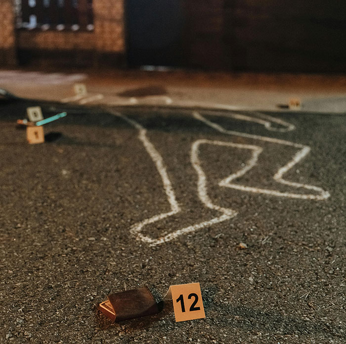Chalk outline of a body on asphalt at a crime scene with evidence markers after a shooting incident in marriage context.