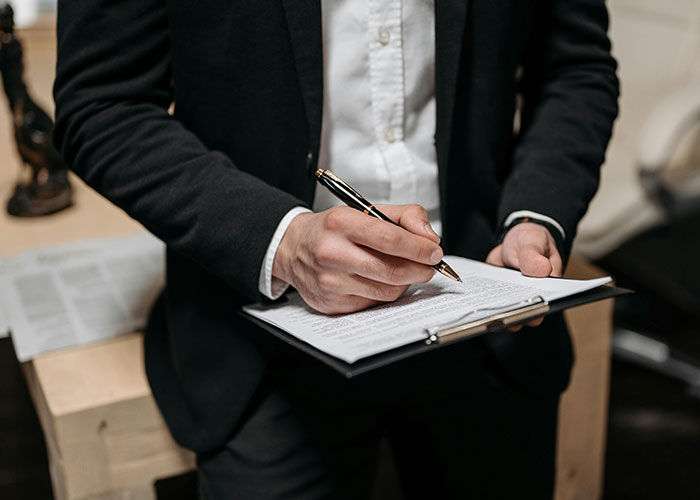 Person in a black suit writing on a clipboard, illustrating a take one for the team moment in a professional setting.