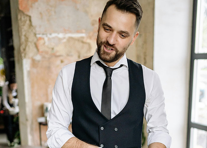 Waitstaff wearing black vest and tie serving guests in a rustic restaurant during awkward and painful dates.