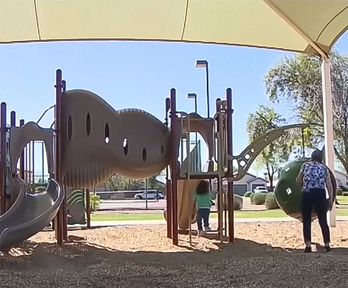 Child playing on playground equipment under shade at a kids park with a mother nearby, related to pickup truck incident.