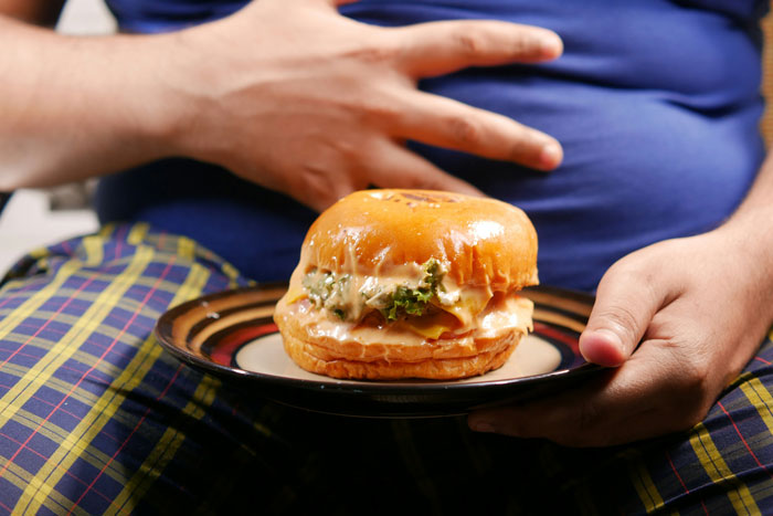 Person holding a cheeseburger on a plate, illustrating the biggest mistake related to unhealthy eating habits.