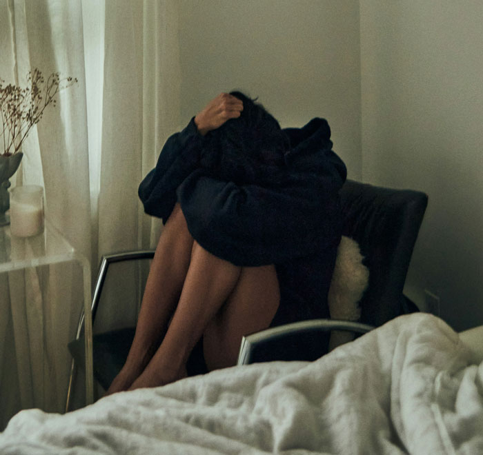 Millennial sitting curled up in chair in dim room, reflecting on biggest lies they were told growing up.