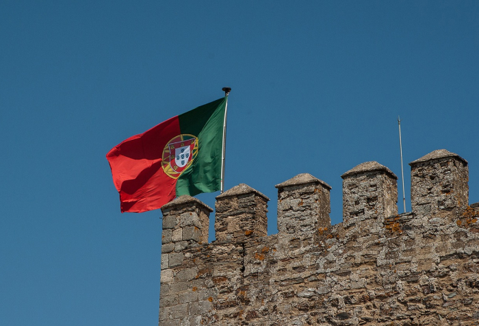 Portuguese flag waving above ancient stone castle wall under clear blue sky representing best countries to live in 2025