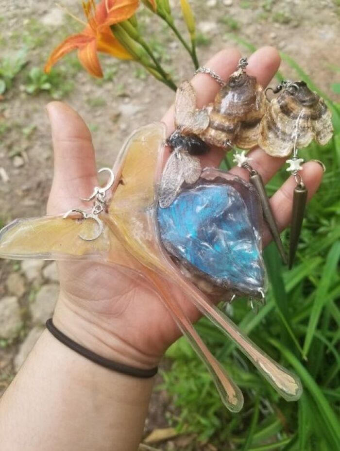 Hand holding failed DIY crafts including butterfly wings and insect earrings in an outdoor setting for craft shaming.