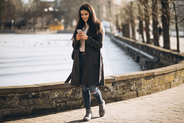 Young woman walking outdoors on a sunny day, wearing a long coat and jeans, with a good trend slowly disappeared vibe.