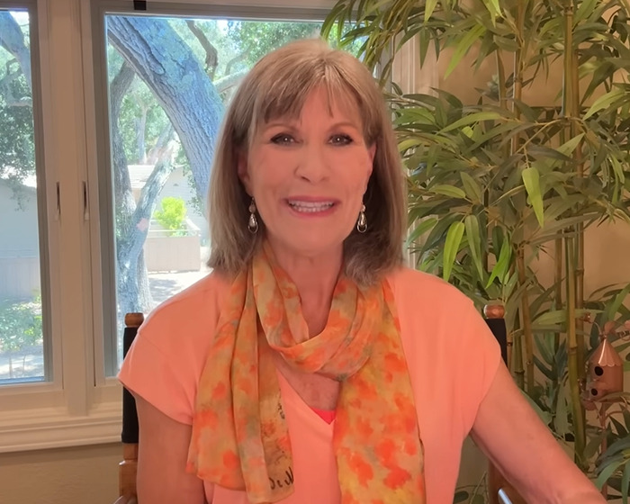 70s TV actress known for bold Playboy shoot wearing orange top and scarf, smiling indoors by window and plants. 70s TV actress known for bold Playboy shoot wearing orange top and scarf, smiling indoors by window and plants.