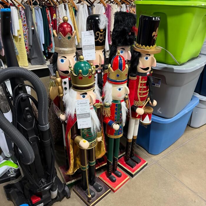 Colorful secondhand nutcracker figurines displayed among clothes and storage bins in a thrift store setting.