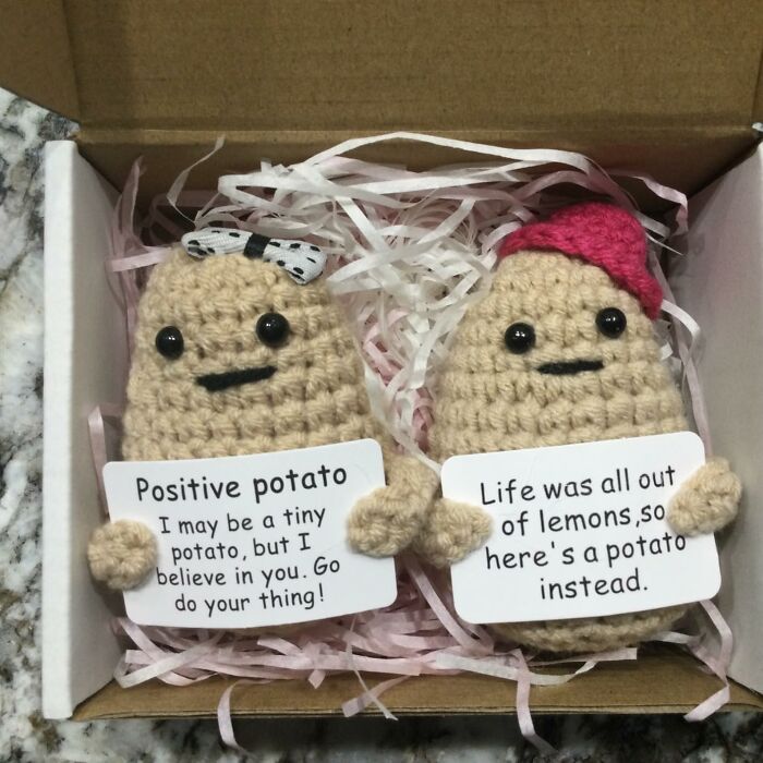 Handmade crochet positive potato dolls holding motivational signs, creative spirit arty finds in a gift box with shredded paper.