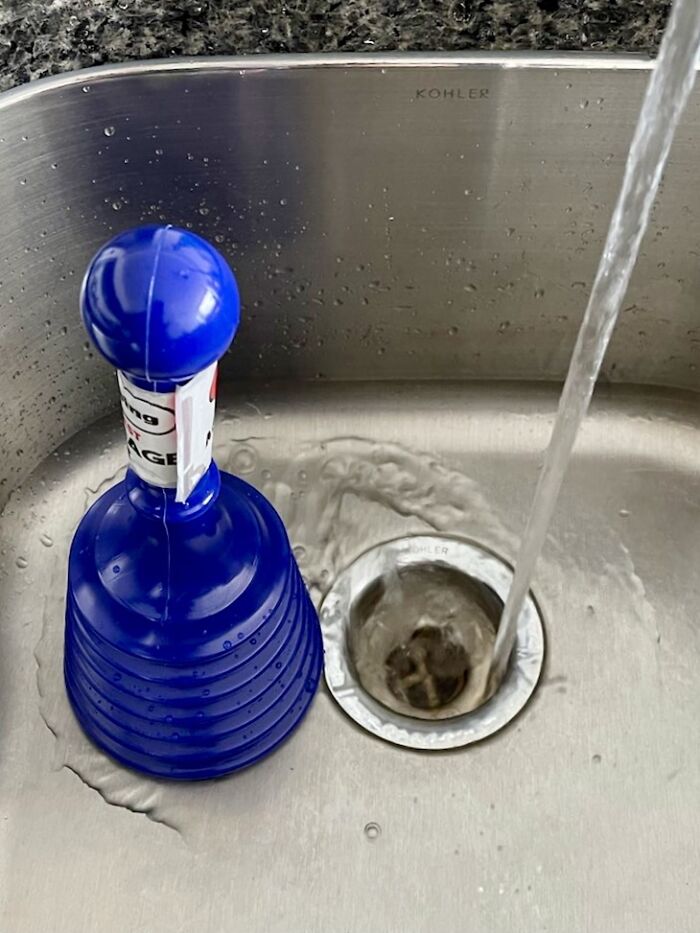 Blue sink plunger in a stainless steel kitchen sink with running water, essential for adulting first apartment care.