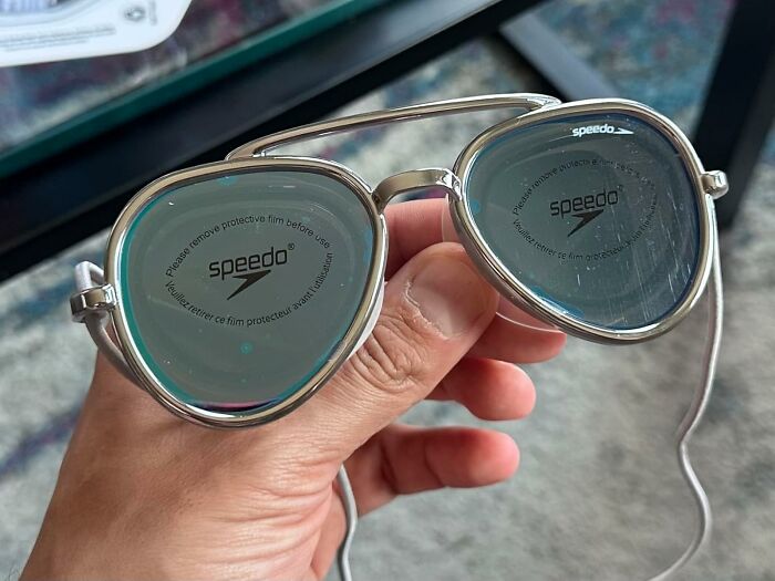 Hand holding Speedo sunglasses with protective film, symbolizing ways to fight back summer annoyances effectively.