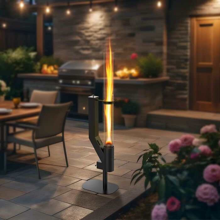 Outdoor space lighting with modern fire torch on patio near dining area and garden at night for usable ambiance.