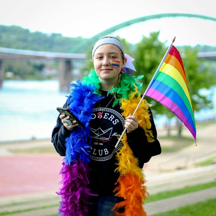 Person wearing colorful feather boas and holding a rainbow pride flag outdoors, showcasing pride pieces for all-year celebration.