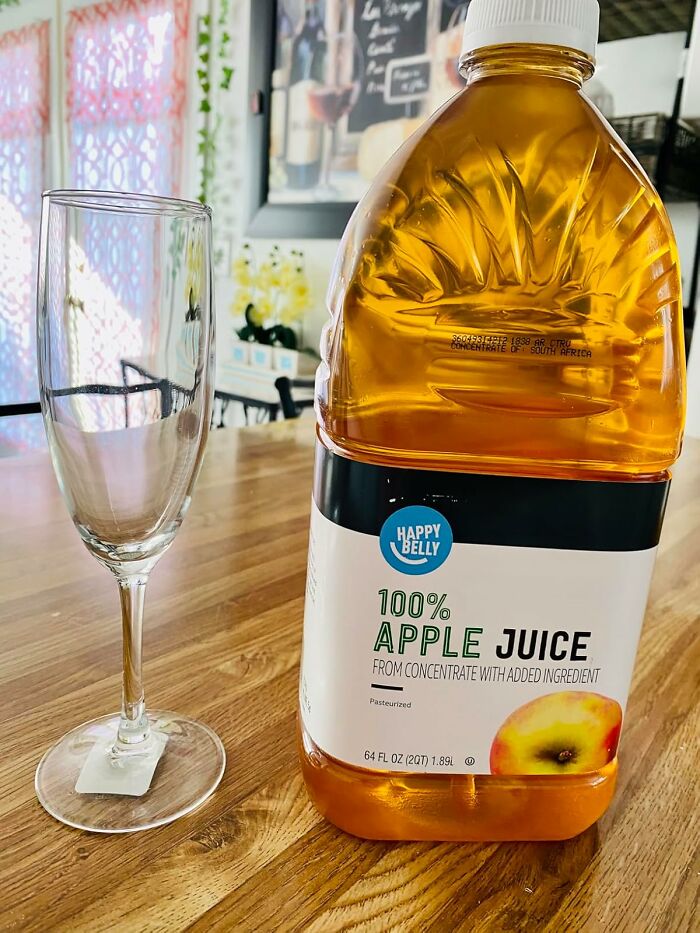 Large bottle of apple juice and empty glass on wooden table highlighting Amazon Fresh staples cheaper than big box stores.