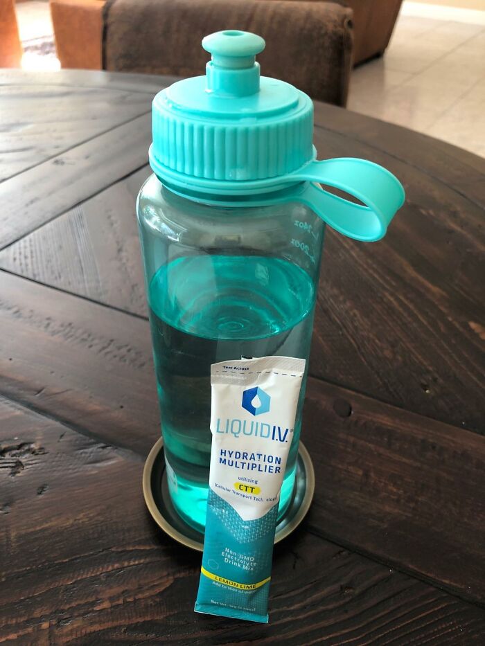 Water bottle with hydration multiplier powder on a wooden table, promoting ways to fight summer annoyances.