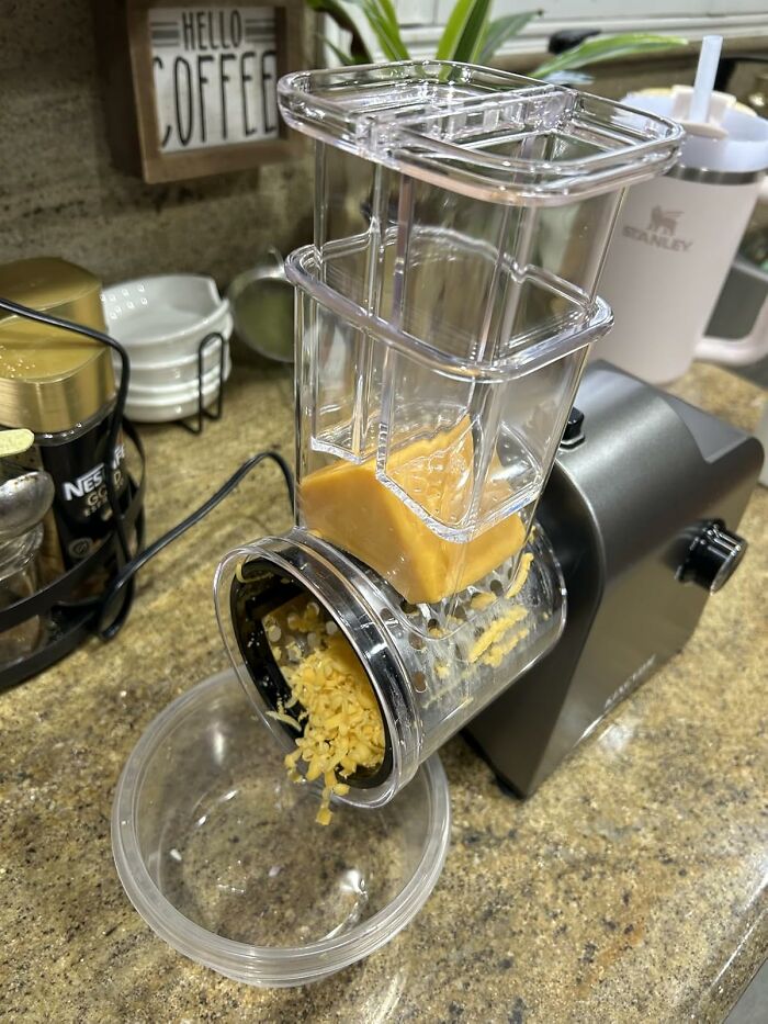 Multi-tasking home kitchen gadget shredding cheese with clear hopper and black base on countertop.