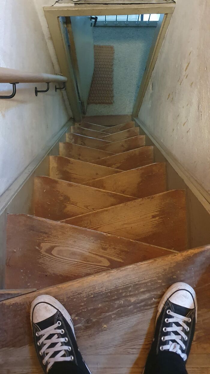 Worn wooden death stairs with narrow, uneven steps and a steep descent viewed from a person's perspective.