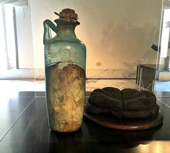 Ancient glass bottle with preserved bread inside, displayed in a museum showcasing archaeology world historical artifacts.