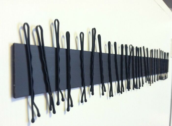 Row of black bobby pins clipped onto a black strip mounted on a white wall, illustrating pregnancy and twins concept.
