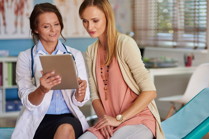 Female doctor and patient reviewing medical information on a tablet, highlighting frustrations with dismissive doctors.