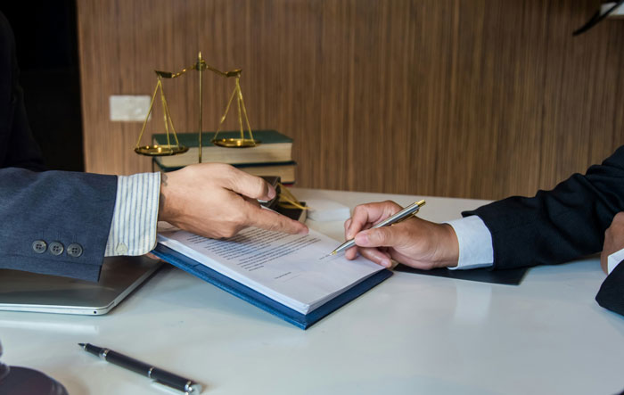 Two men in suits reviewing documents on a table with legal scales and books, related to hired PI findings.