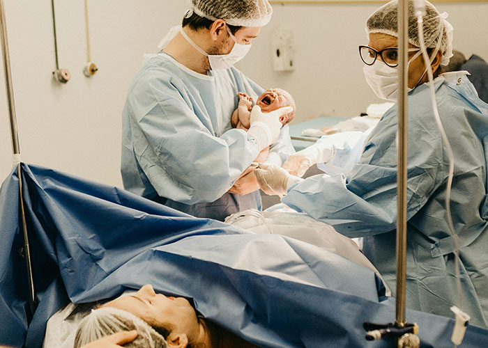 Medical staff in protective gear assist in the birthing room as a dad witnesses the newborn’s first moments.
