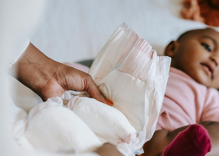 Hand holding a diaper near a baby lying down, depicting everyday care moments for parents and children.
