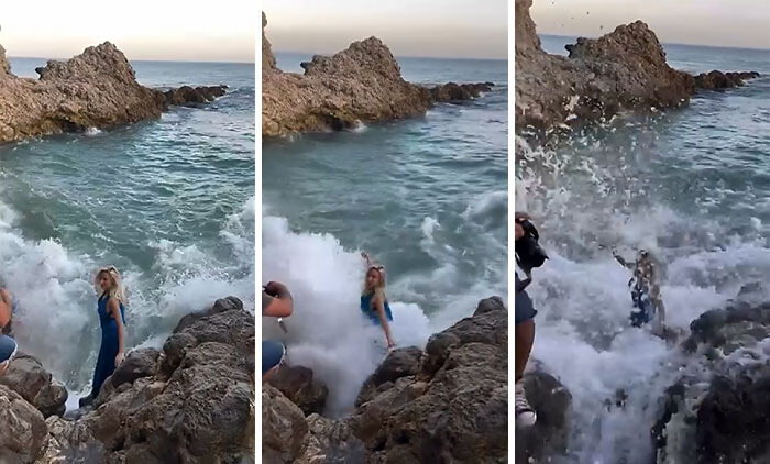 Influencer standing on rocks near ocean gets hit by a large wave while filming for views and unhinged content.
