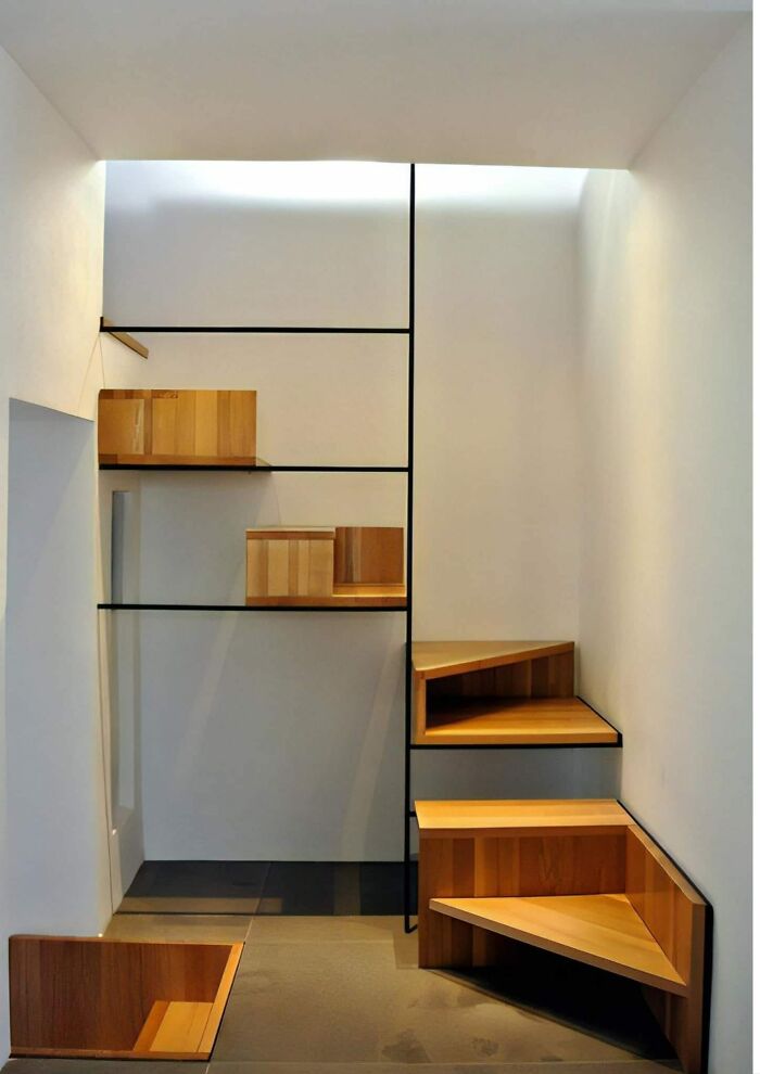 Modern wooden death stairs with sharp turns and minimalistic design inside a white room with black trim accents.