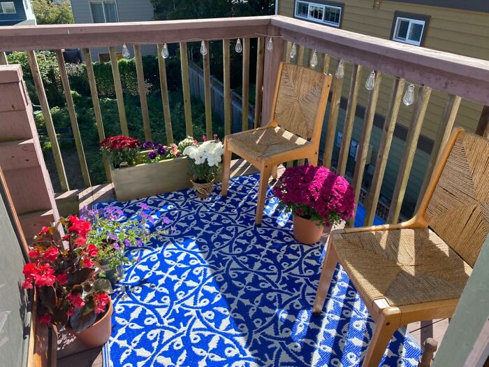 Small balcony area with colorful flowers and patterned rug used to hide ugly eyesores in home outdoor space.