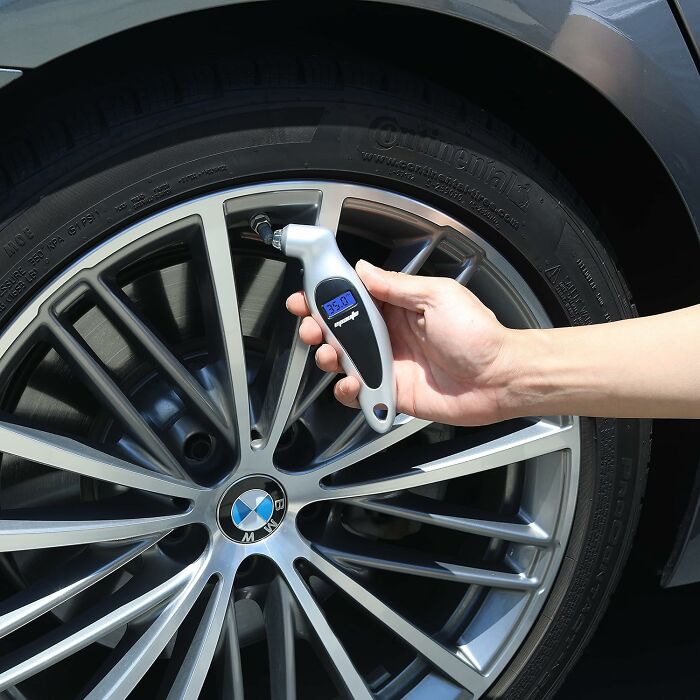 Hand using a digital tire pressure gauge on a BMW car wheel, showcasing clever car finds for better commute preparation.