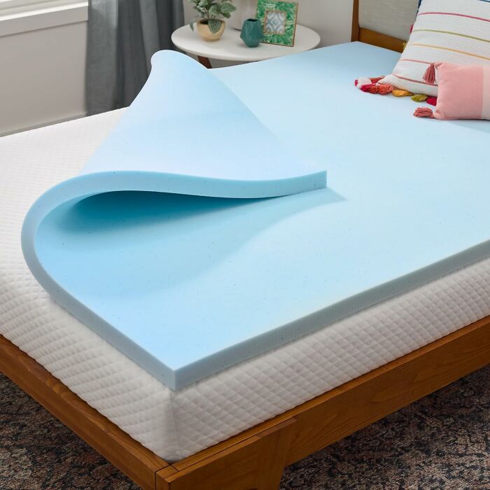 Blue memory foam mattress topper partially rolled up on bed frame, highlighting early Prime Day deals for home comfort products.
