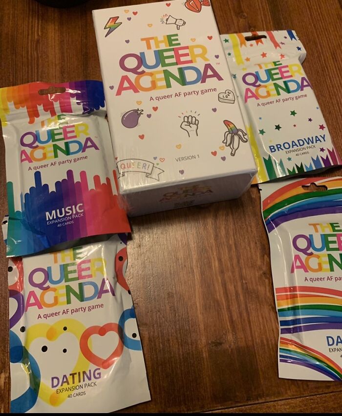 The Queer Agenda game and colorful pride-themed expansion packs arranged on a wooden surface for all year pride celebration.