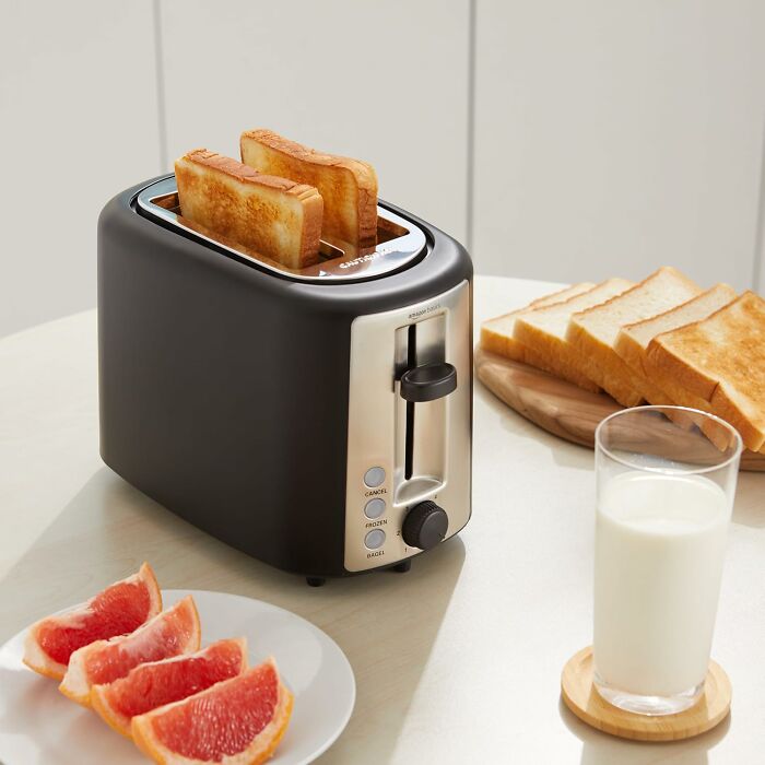 Black toaster with toasted bread slices, grapefruit wedges on a plate, and a glass of milk on the table, budget-friendly deals.