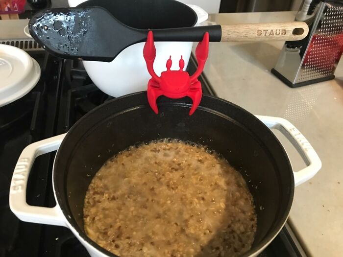 Red crab spoon rest holding cooking spatula over pot on stove, adulting starter pack kitchen essential for first apartment.