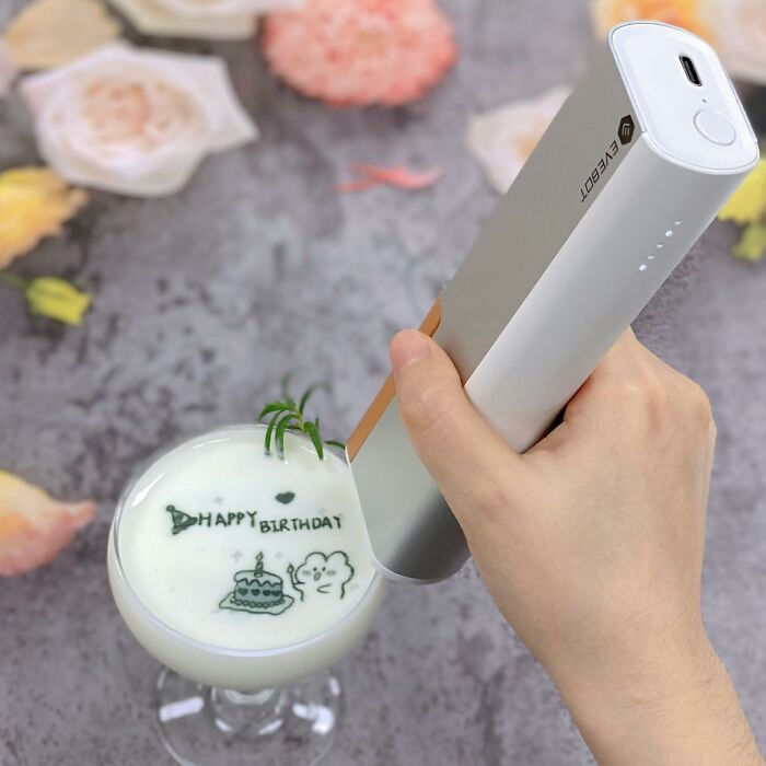 Hand using a crafting kit to draw detailed art on foam in a birthday-themed drink, showcasing creative crafting tools.