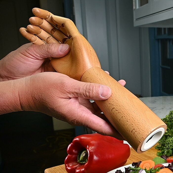 Wooden hand-shaped kitchen gadget held above chopped vegetables and a red bell pepper on a cutting board.