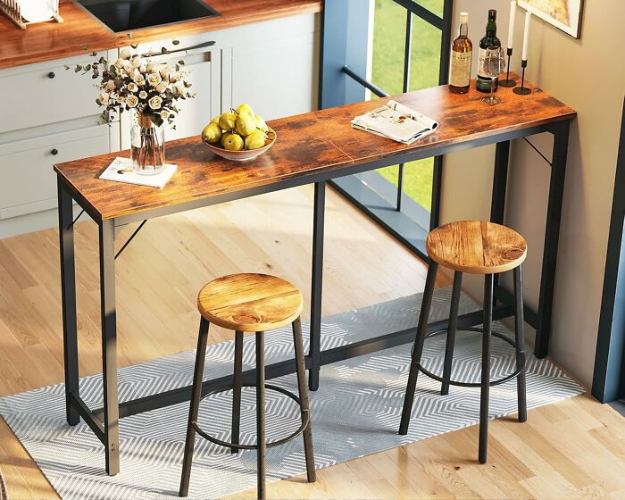 Rustic wooden kitchen bar table with two stools, bottles, fruit bowl, and decor, perfect for prime day kitchen finds.
