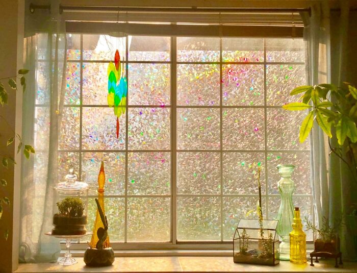 Window decorated with colorful stained glass and plants, showcasing creative ways to hide the ugliest eyesores in your home.